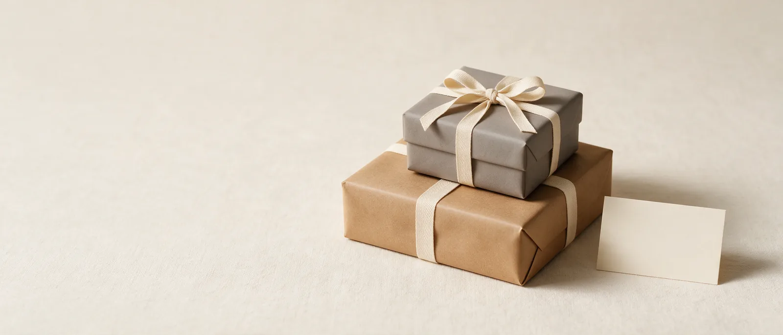 Two wrapped gifts tied
with cream ribbon beside a small note card on a linen surface