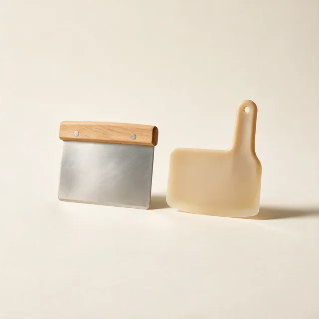 A metal bench scraper beside a plastic dough scraper