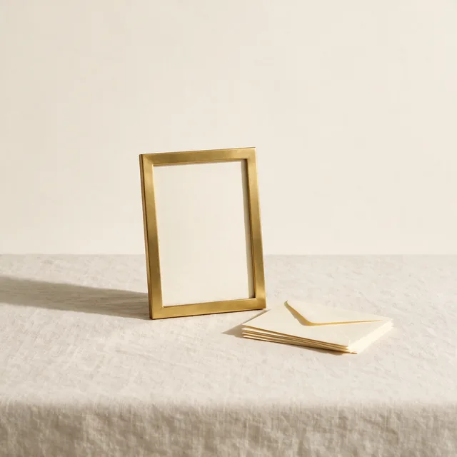 An empty brass picture frame beside a stack of cream envelopes