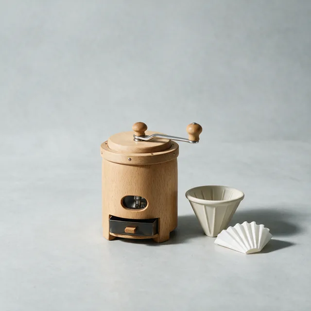 A hand coffee grinder beside a pour over cone and a filter