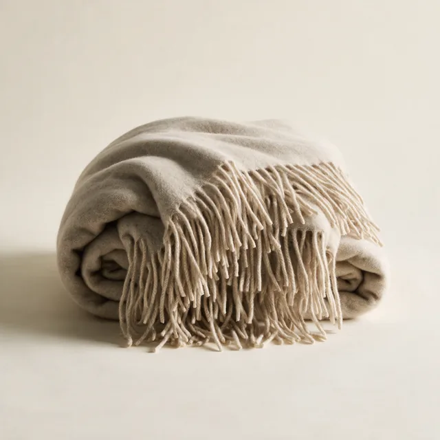 A thickly folded wool throw blanket with a fringed edge