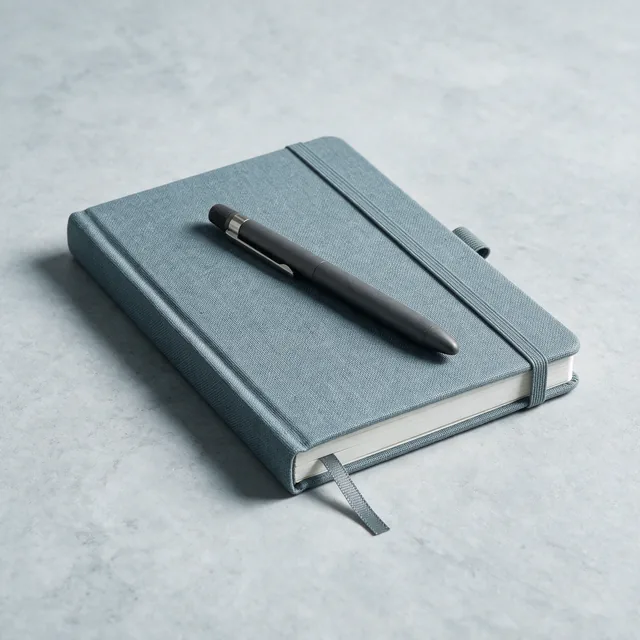 A slate cloth hardcover notebook with a matte pen resting on it