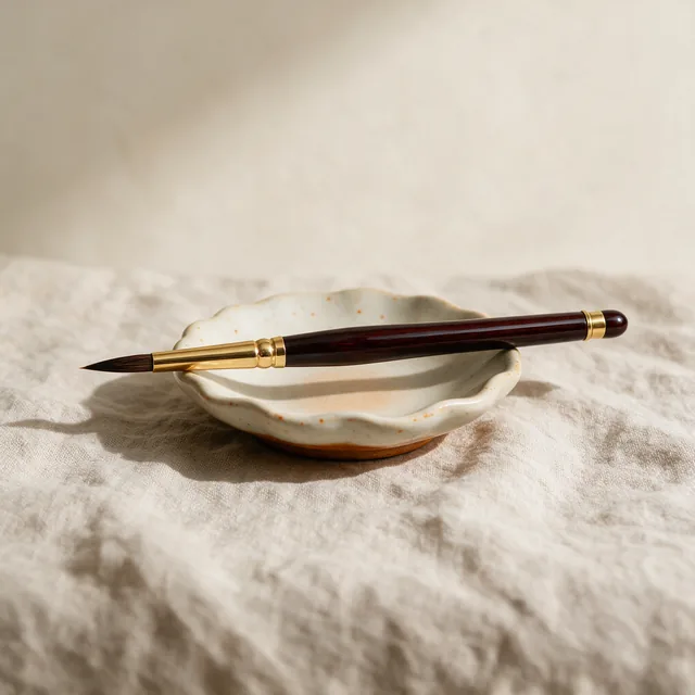 A fine sable paintbrush resting across a ceramic dish