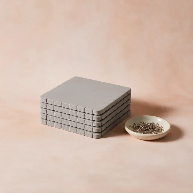 A stack of foam blocking mats with a dish of T-pins