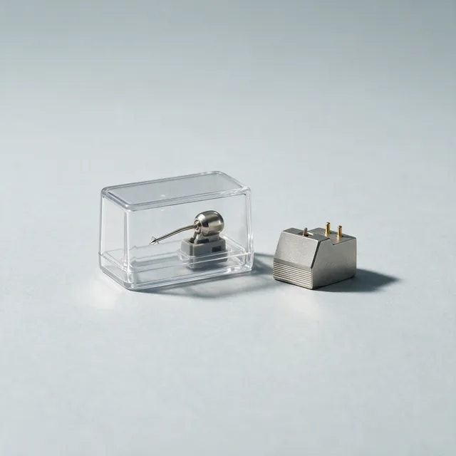 A replacement turntable stylus in a clear case beside a cartridge