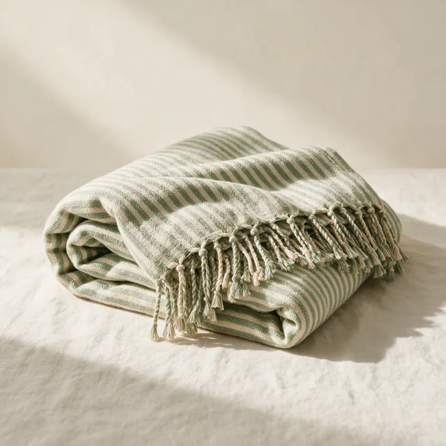 A folded striped cotton yoga blanket with a fringed edge