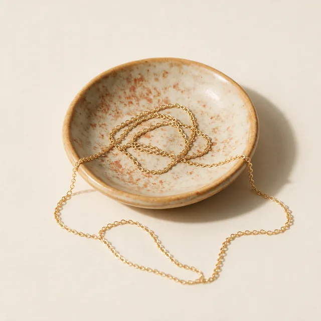 A thin gold chain necklace coiled on a ceramic dish