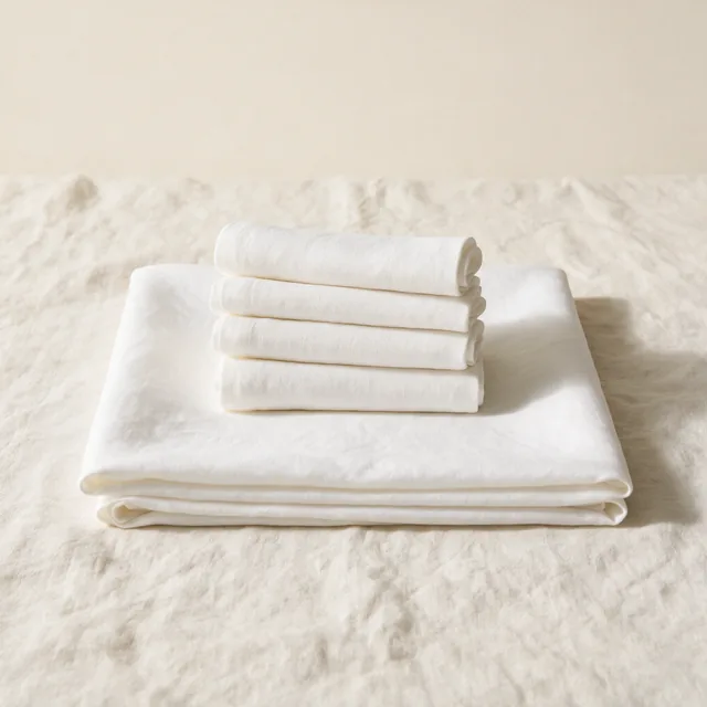 A folded linen tablecloth with rolled napkins stacked on top