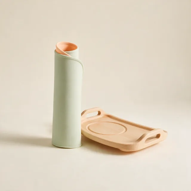 A rolled silicone splash mat beside a wooden high chair tray